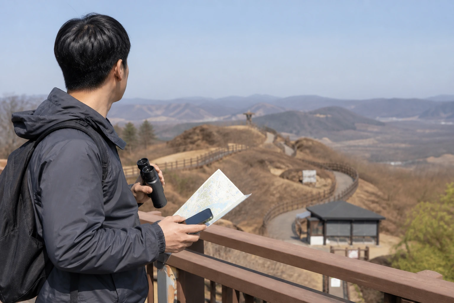 바람막이를 입은 여행자가 쌍안경과 예약 확인용 스마트폰을 들고 도라전망대 방향을 바라보는 DMZ 준비 장면